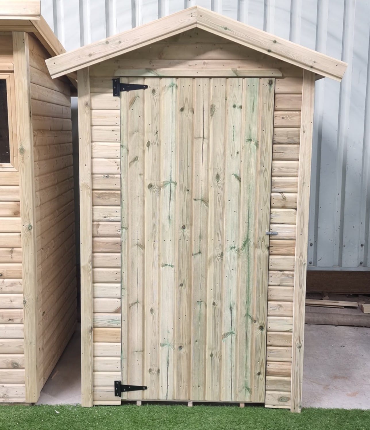 A 1200mm x 1200mm (4ft x 4ft) Apex shed with shiplap boards and a green mineral polyester felt roof, set in a garden with illustrative wheelbarrows, plants, and tools.
